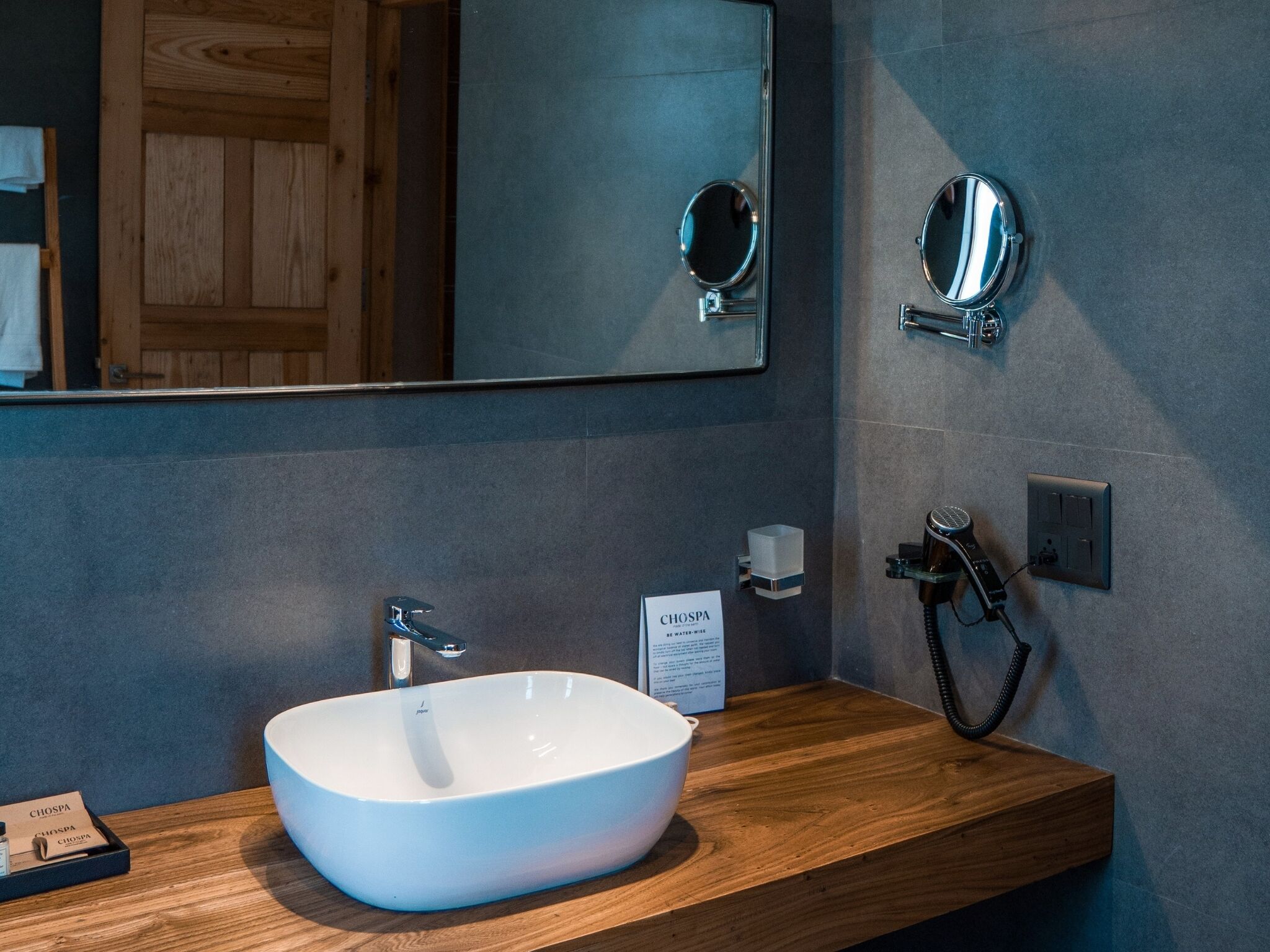 Un baño con lavamanos blanco, tocador de madera, un espejo grande y un perchero para toallas.