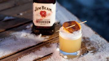Una botella de Jim Beam Bourbon y un vaso con un cóctel sobre una mesa de madera cubierta de nieve.
