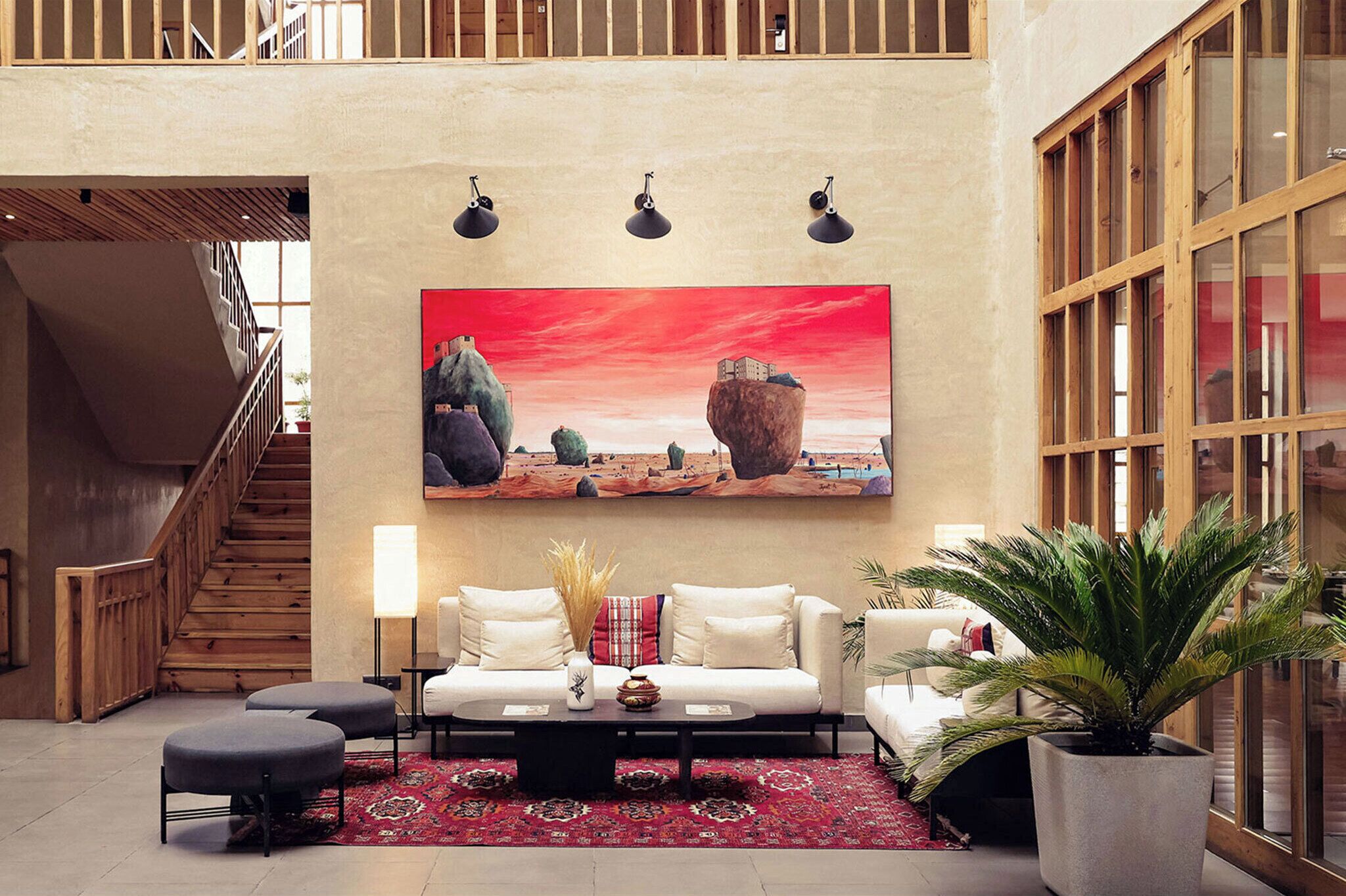 A spacious lobby with a modern staircase, a large painting of a desert landscape, a white sofa, and a potted plant.