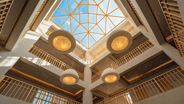 A multi-level atrium with a geometric glass ceiling, wooden railings, and circular light fixtures. - Chospa Hotel (Leh)