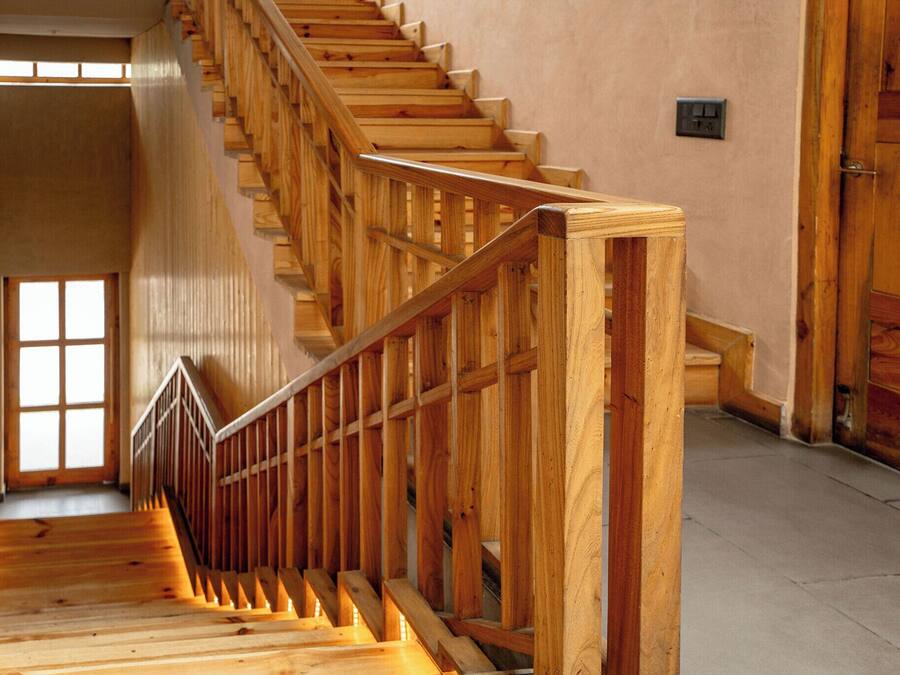 A wooden staircase with a handrail, leading to a room with a door and a light switch on the wall.