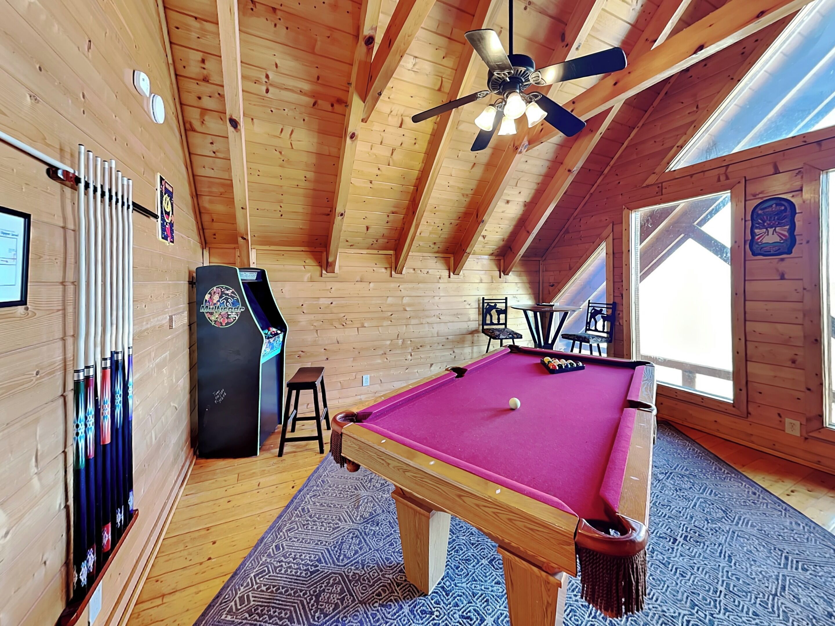 A pool table in a wooden room with a ceiling fan, a pool table, and a pool table with a ball.