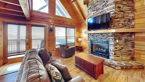 A cozy cabin interior with a stone fireplace, wooden walls, and a leather sofa.