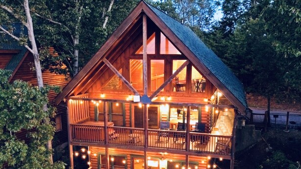 A two-story log cabin with a balcony, surrounded by trees.