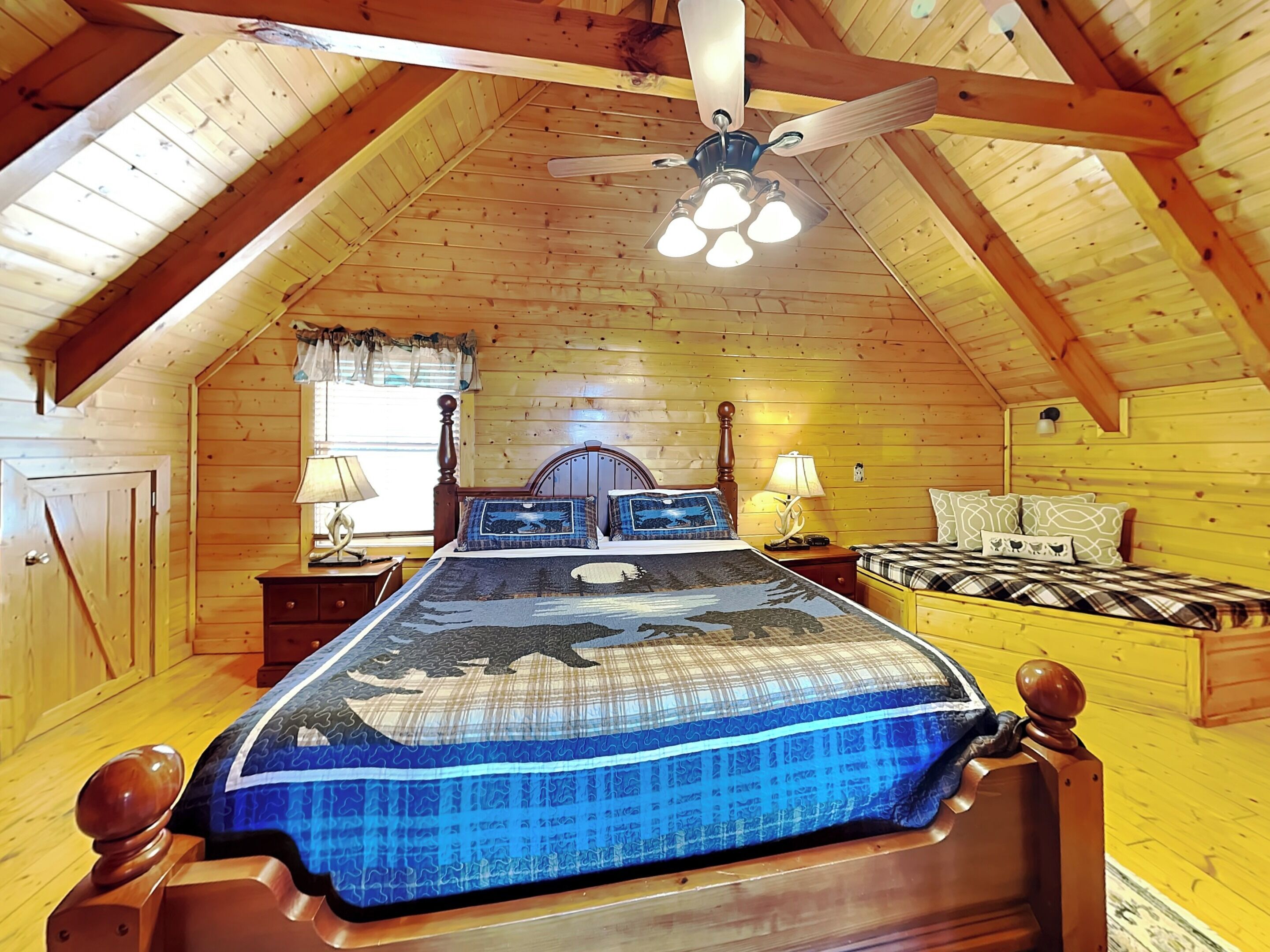 Un dormitorio de cabaña de madera acogedor, con una cama, dos mesitas de noche, un ventilador de techo y una ventana con cortinas.