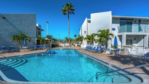 A swimming pool with clear blue water, surrounded by lounge chairs and palm trees. - Madeira Beach Yacht Club 151H by Distinctive Beach Rentals (Madeira Beach)