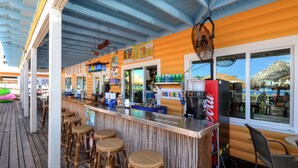 A bar area with a counter, stools, and a view of the sea through large windows. - Madeira Beach Yacht Club 151H by Distinctive Beach Rentals (Madeira Beach)