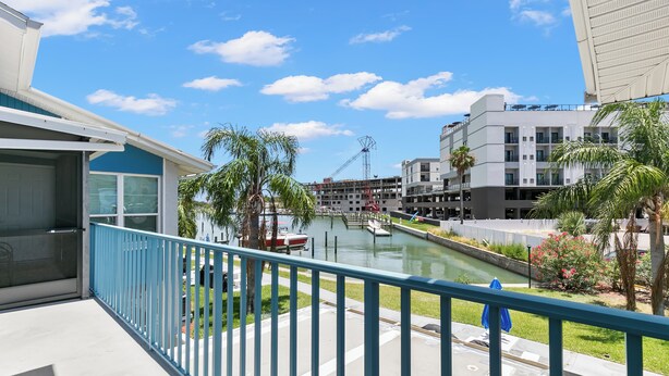 A balcony with a view of a canal, palm trees, and a construction crane in the background. - Madeira Beach Yacht Club 151H by Distinctive Beach Rentals (Madeira Beach)