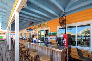 A bar area with a counter, stools, and a view of the sea through large windows. - Madeira Beach Yacht Club 151H by Distinctive Beach Rentals (Madeira Beach)