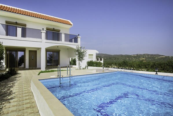 A modern two-story house with a swimming pool, large windows, and a view of the countryside.