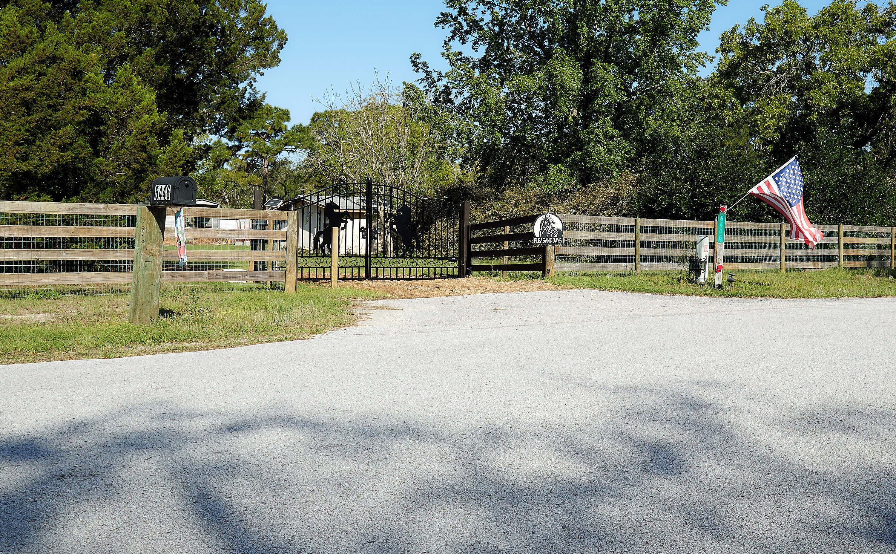 A gated entrance with a metal gate, a wooden fence, and an American flag.