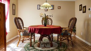 A dining area with a round table, four wicker chairs, a red tablecloth, a decorative vase, and a hanging lamp. - Pleasant Days Manatee Room (Homosassa)