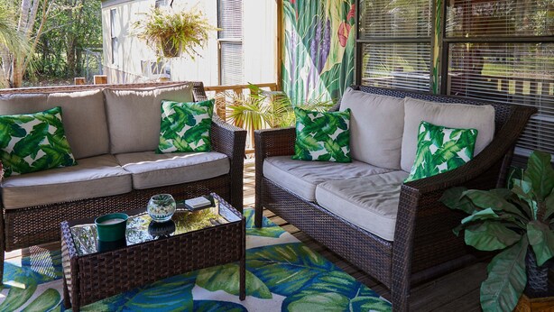 A wicker sofa with cushions, a glass coffee table, and a patterned rug in a sunlit room with a view of greenery outside. - Pleasant Days Manatee Room (Homosassa)