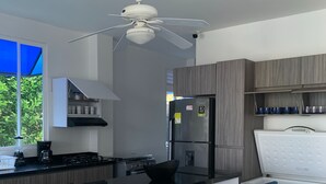 A modern kitchen with a central island, bar stools, a refrigerator, and a ceiling fan.