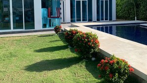 A modern two-story house with a swimming pool, large windows, and a well-maintained lawn.