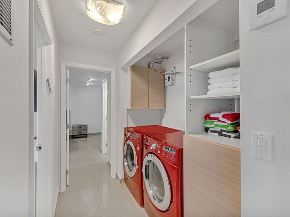 A laundry room with two front-loading washing machines, a wooden cabinet above, and a shelf with folded towels.