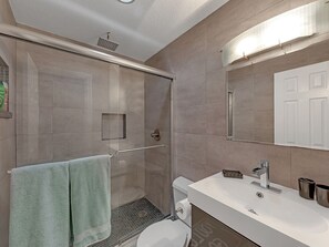 A modern bathroom with a glass shower enclosure, a white sink, and a large mirror.