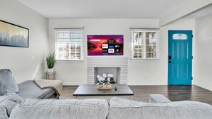A living room with a flat-screen TV mounted above a fireplace, a blue door, and a grey sofa.