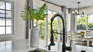 A kitchen with a modern faucet, a white vase with a plant, and a view of the outdoors through large windows.