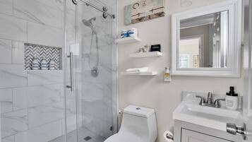 A modern bathroom with a glass-enclosed shower, a toilet, and a sink with hand soap.