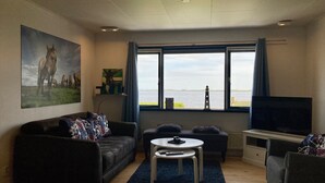 Un salon comprenant un canapé, une table basse, un téléviseur et une grande fenêtre donnant sur l’eau.