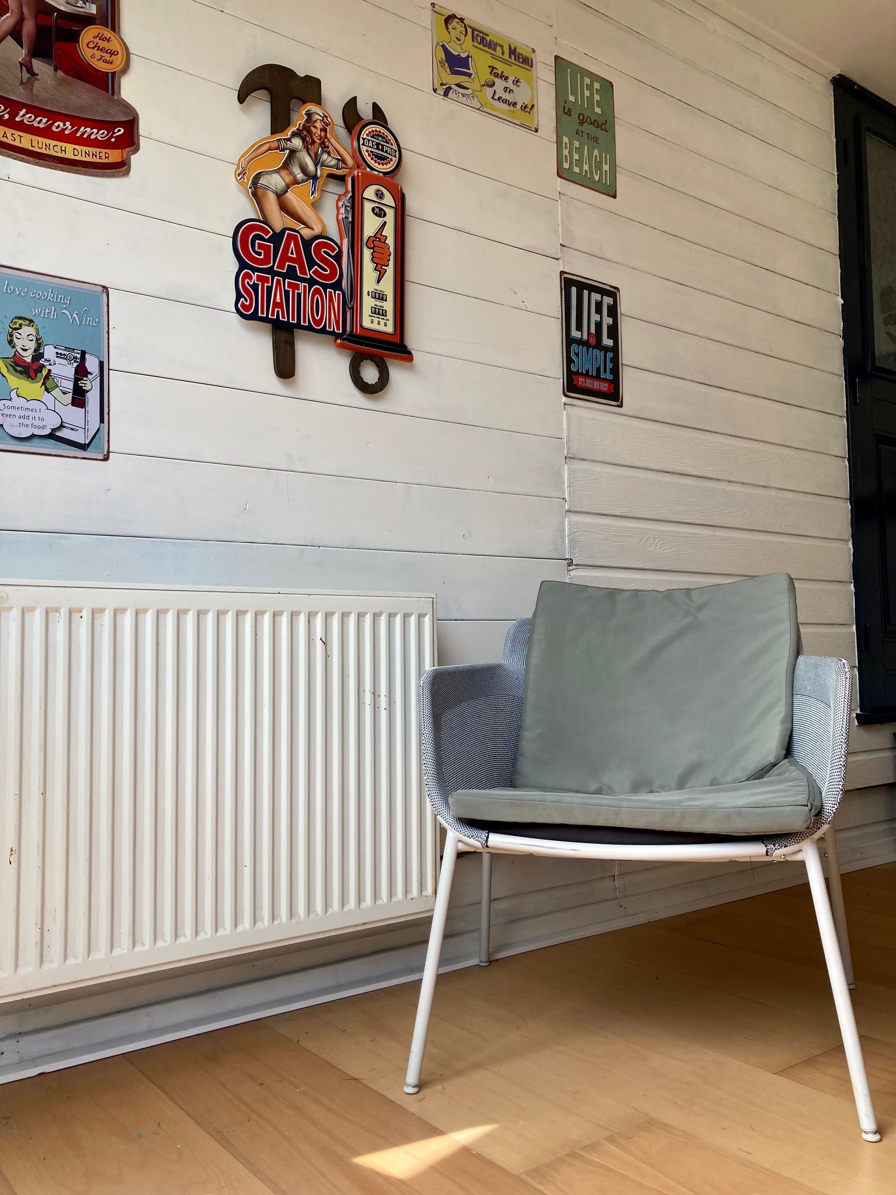 A room with a radiator, a chair, and various wall decorations including signs for a gas station and a beach.