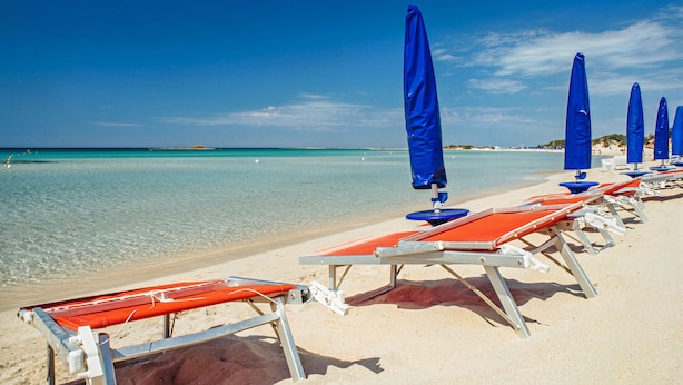 A beach with rows of sun loungers and blue umbrellas, clear turquoise water, and a sandy shore. - Relais With Swimming Pool in Porto Cesareo Torre Chianca (Porto Cesareo)
