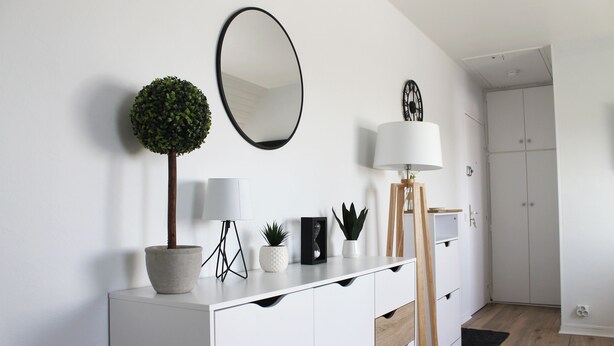 A modern, minimalist room with a white console table, a round mirror, a potted plant, a lamp, and a wardrobe. - Cabourg - Cosy studio 1 min from the beach (Cabourg)