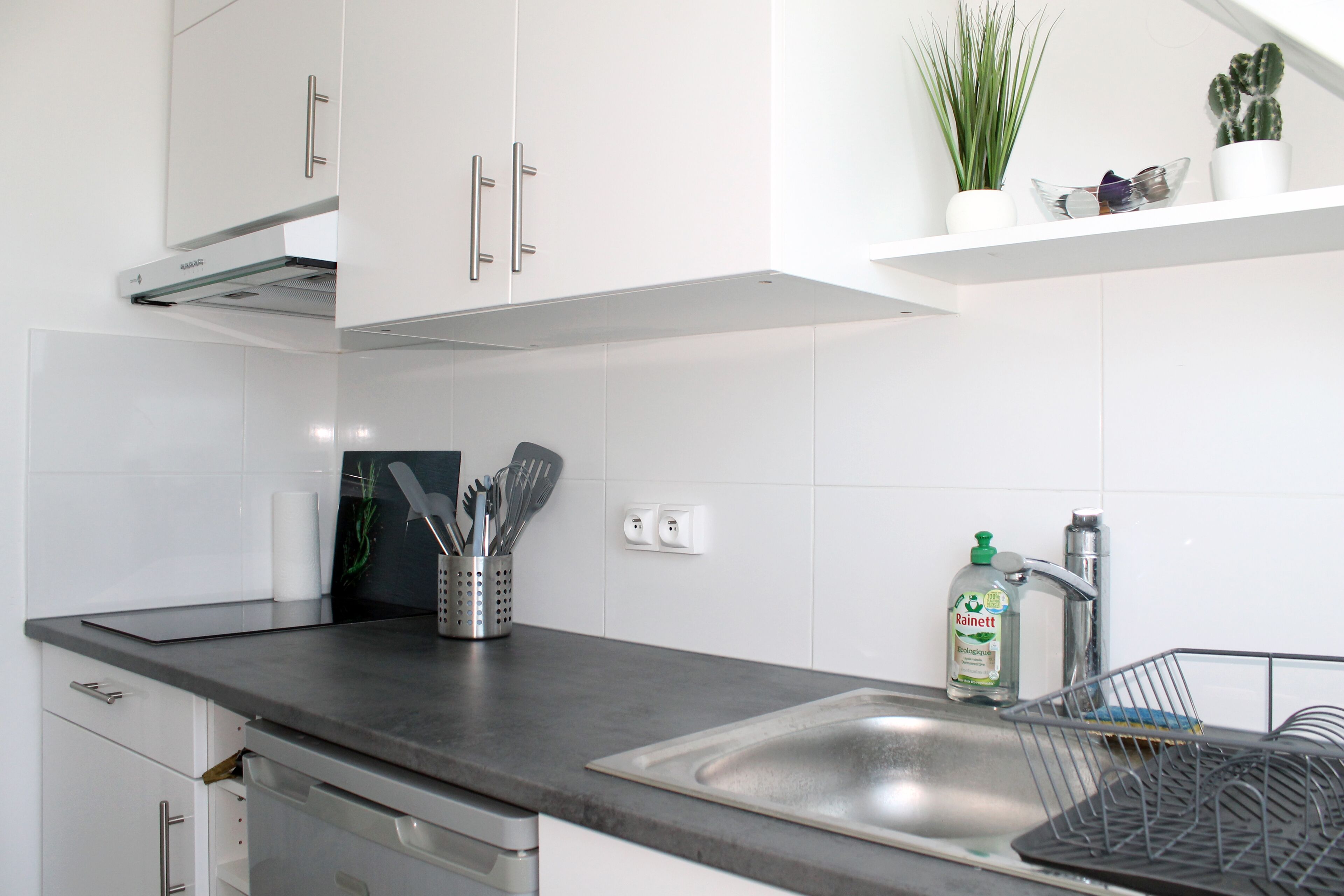 A modern kitchen with white cabinets, a stainless steel sink, and a dish rack.