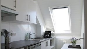 A modern kitchen with white cabinetry, a dishwasher, and a window above the sink. - Cabourg - Cosy studio 1 min from the beach (Cabourg)