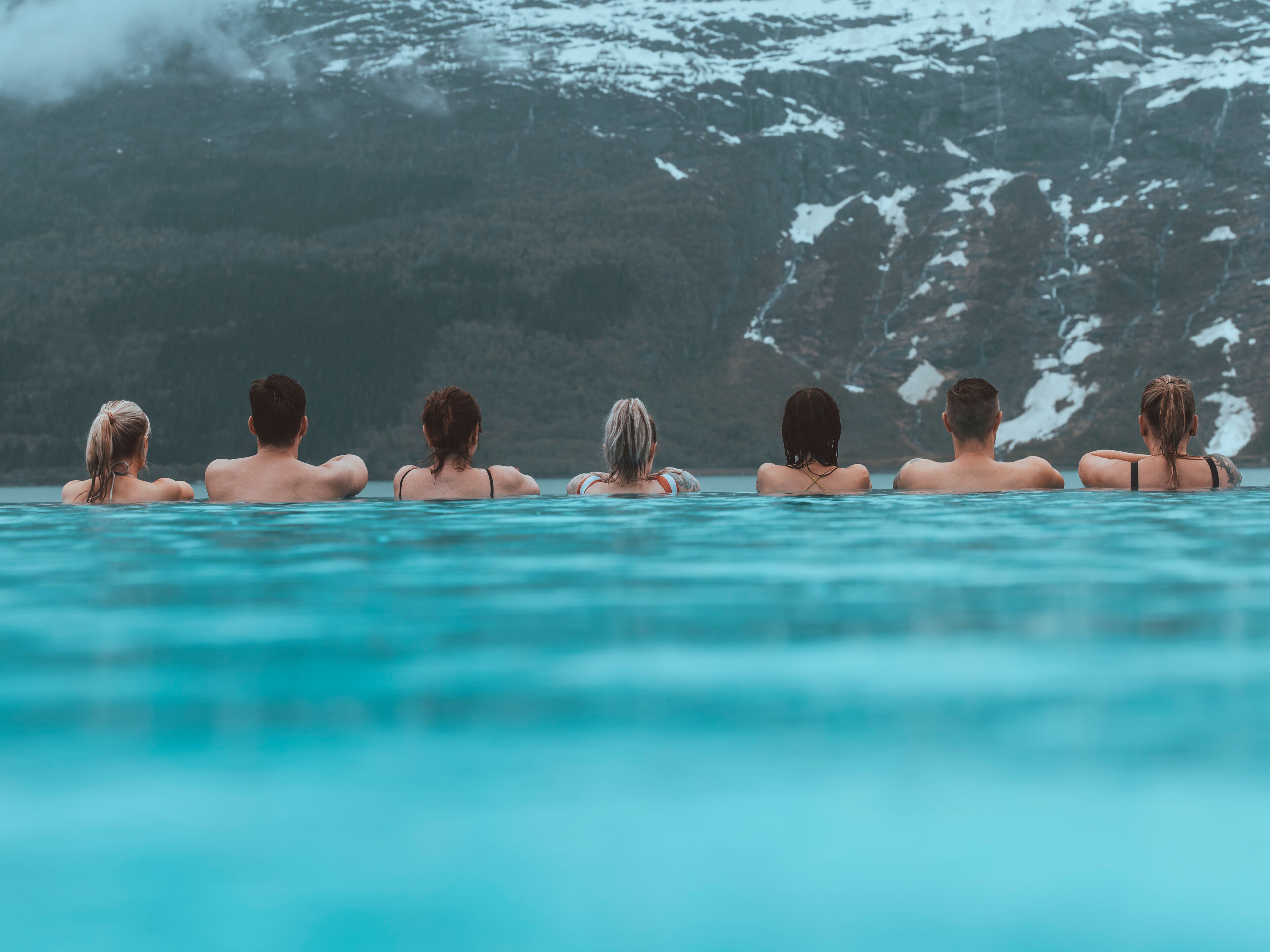 A group of people in a swimming pool with a mountainous backdrop.