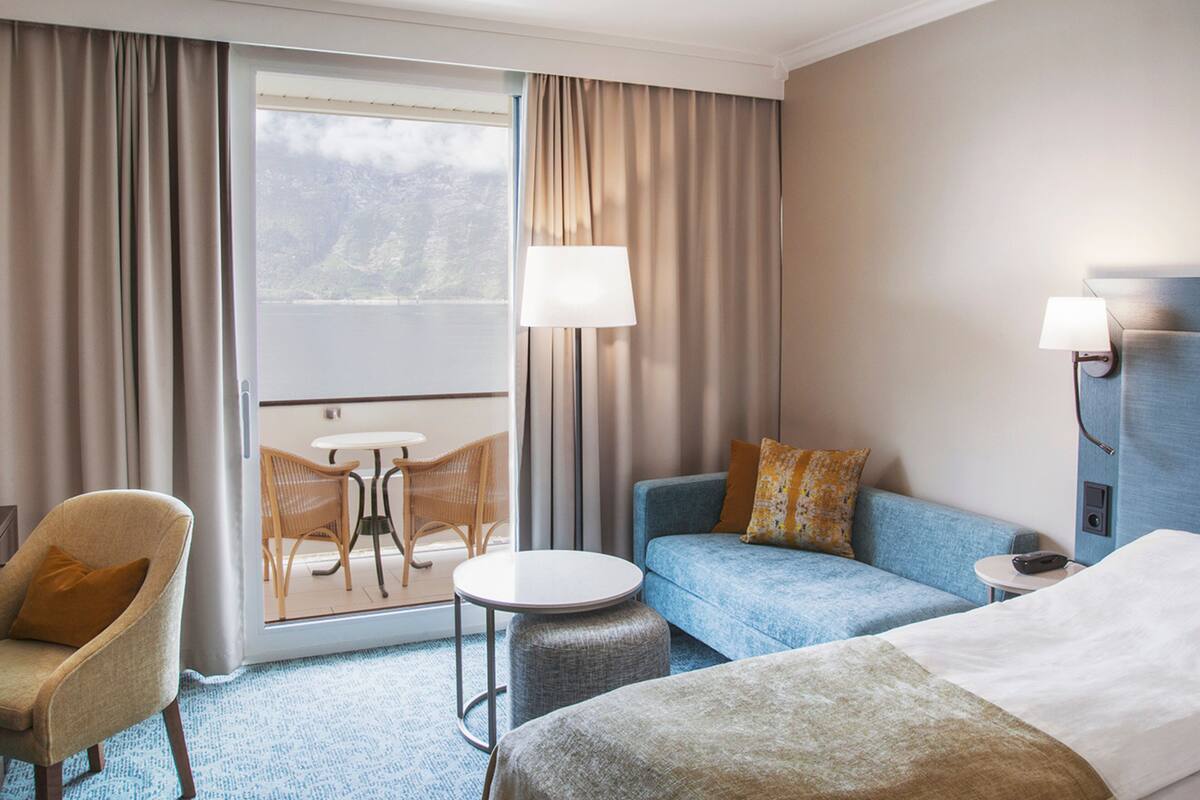 A hotel room with a bed, a sofa, a chair, a small table, and a window with curtains.