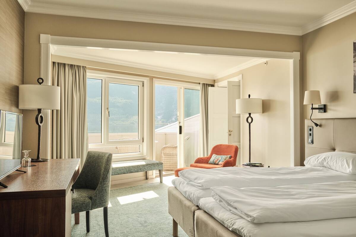 A hotel room with a bed, a desk, a chair, a lamp, and a window with curtains.