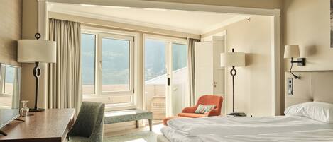 A hotel room with a bed, a desk, a chair, a lamp, and a window with curtains.