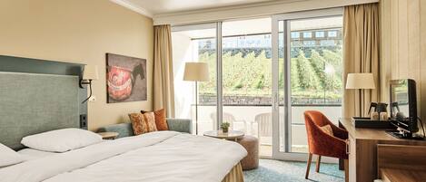 A hotel room with a large bed, a desk, a chair, and a balcony with a view of the outdoors.