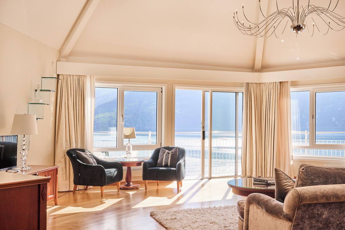 A spacious living room with a large window, a chandelier, and a view of the sea.