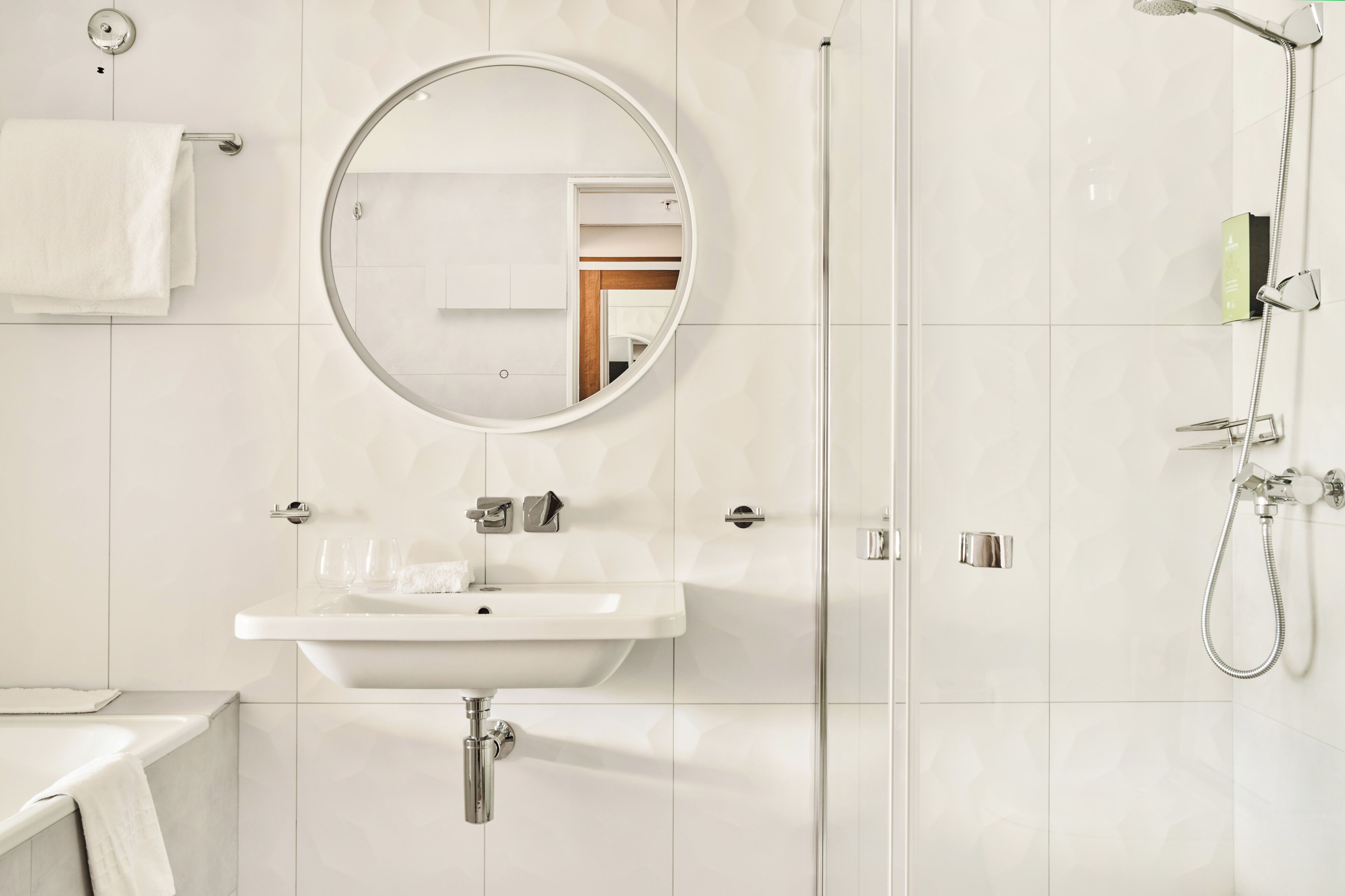 A modern bathroom with a round mirror, a sink, a shower, and a towel rack.