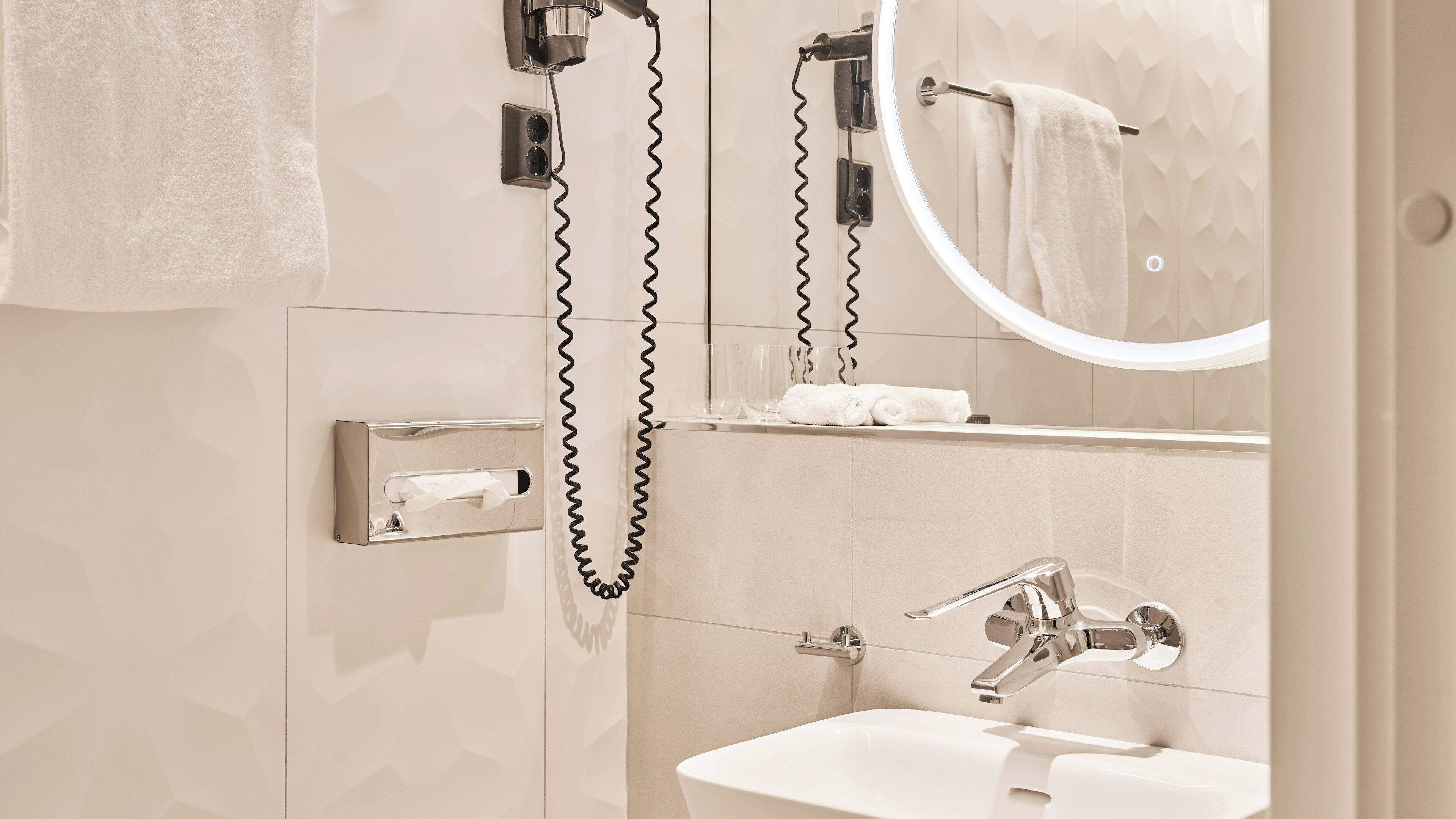 A modern bathroom with a sink, mirror, towel rack, and a hairdryer.