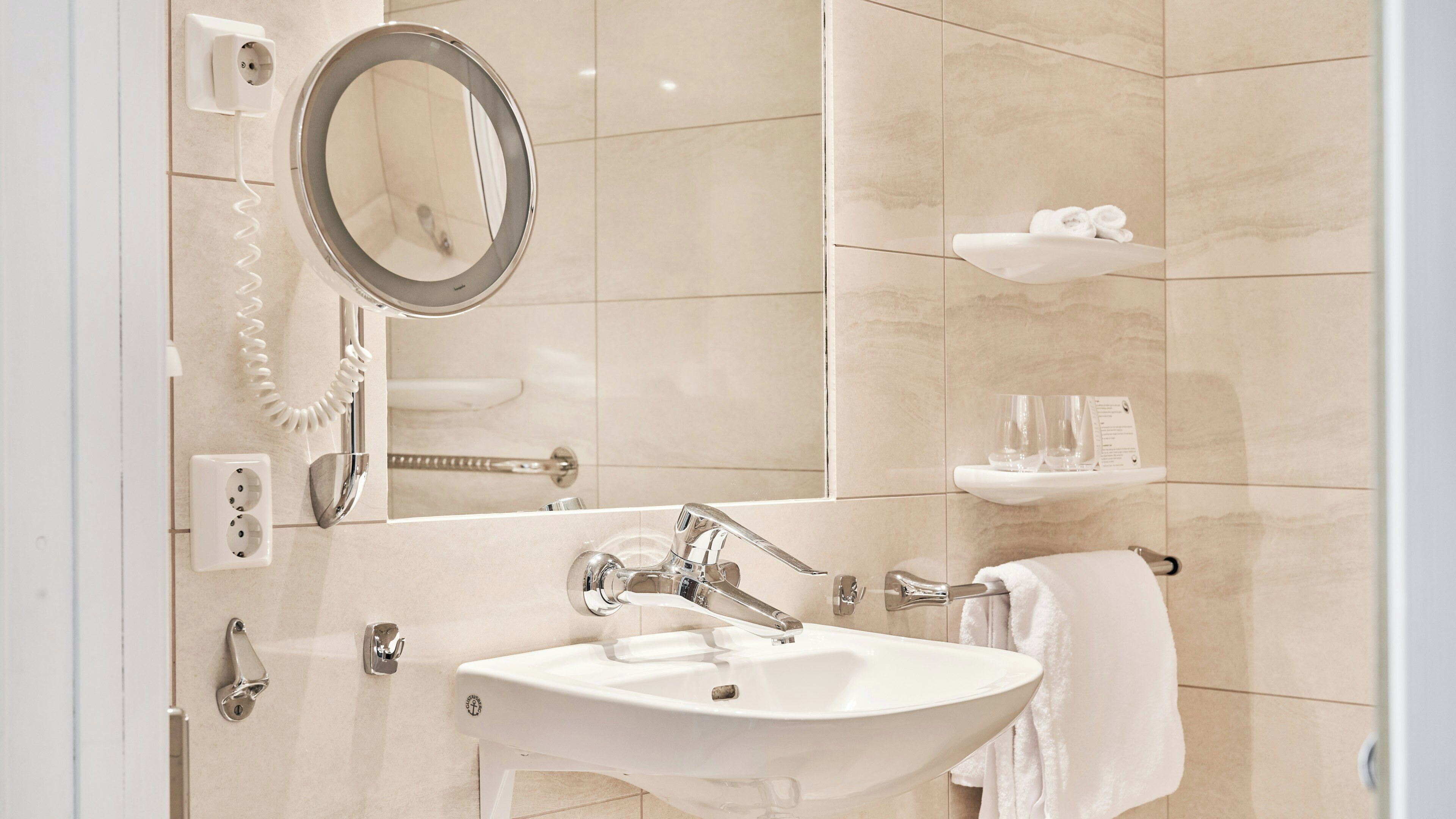 A bathroom with a white sink, mirror, towel rack, and a shelf with toiletries.