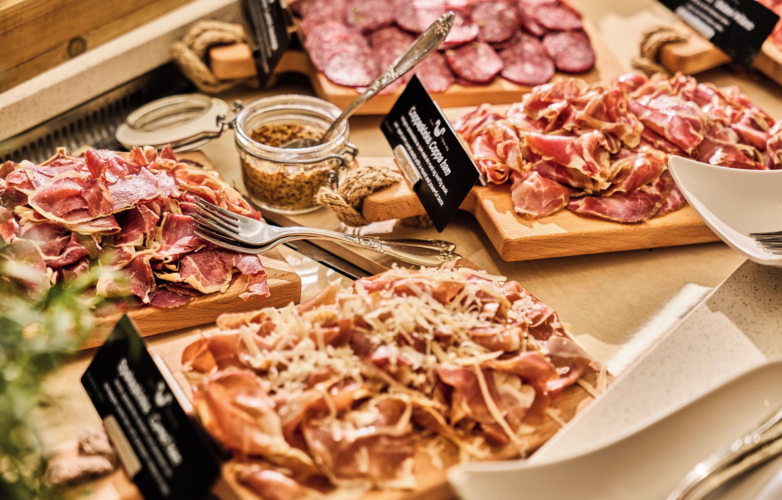 Une variété de charcuteries et de fromages présentés sur des planches en bois, accompagnés d’étiquettes.