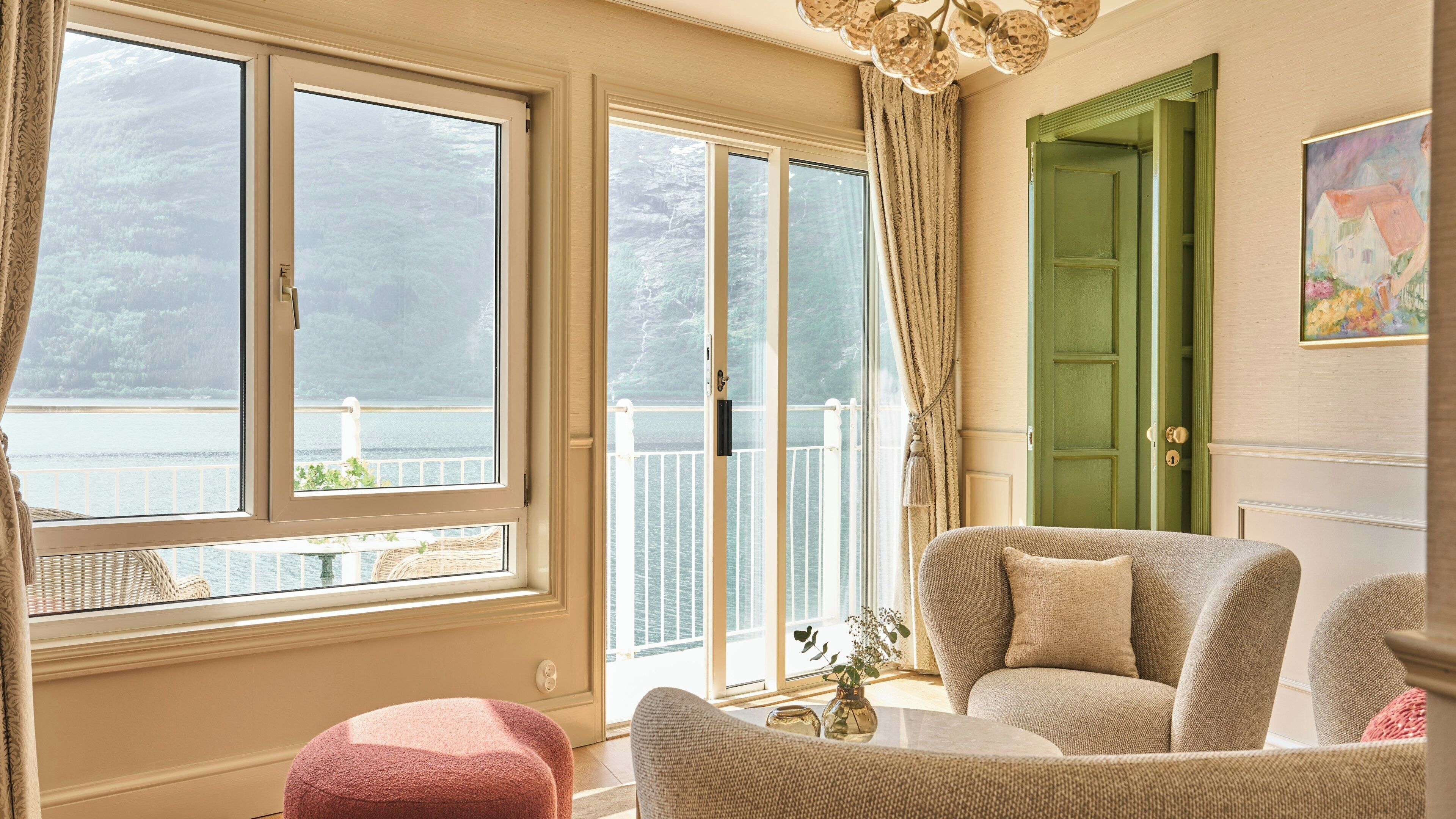 A room with a view of the sea, a green door, and a chair with a cushion.