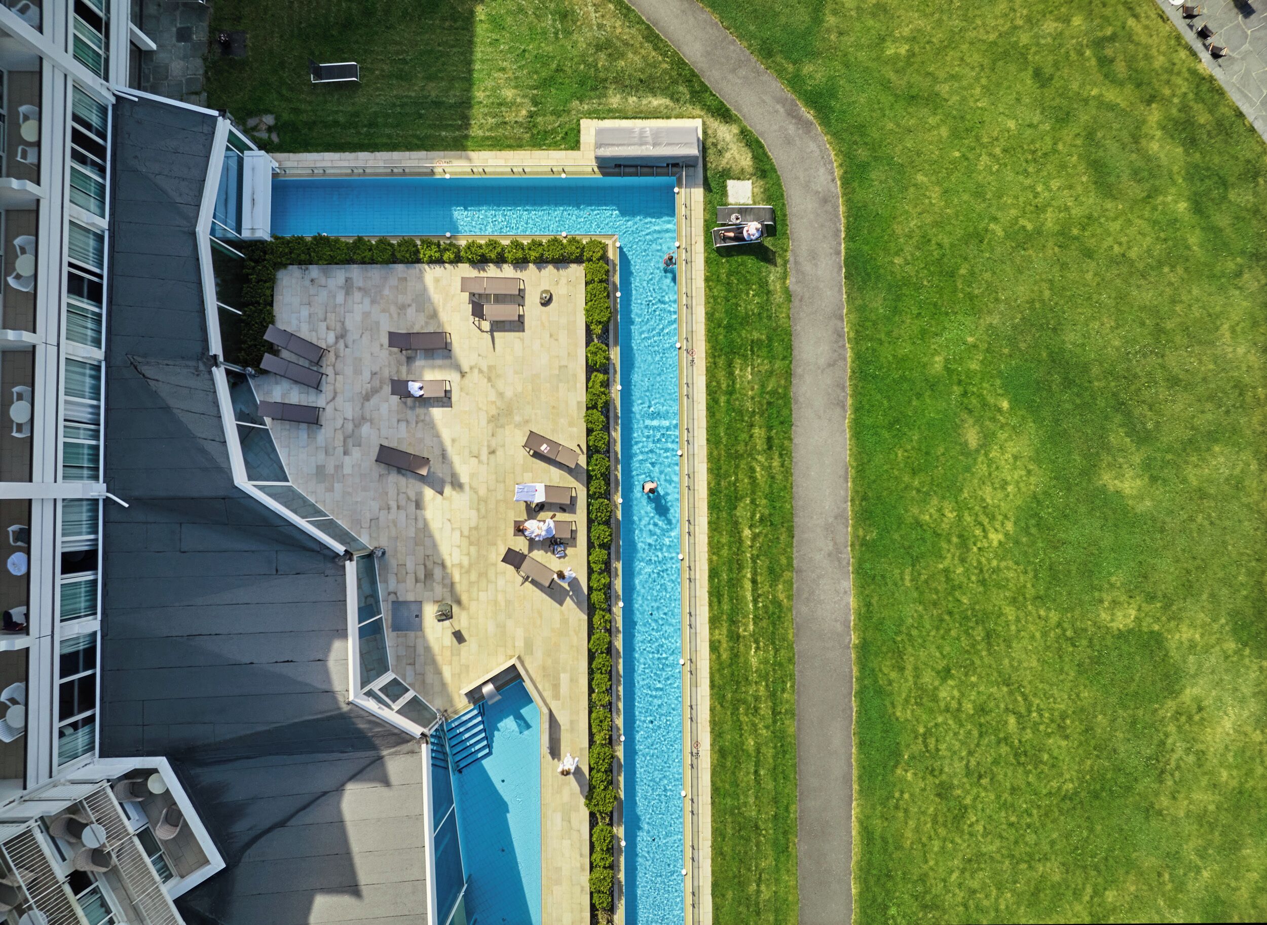 An aerial view of a hotel with a swimming pool, lounge chairs, and a paved deck area.