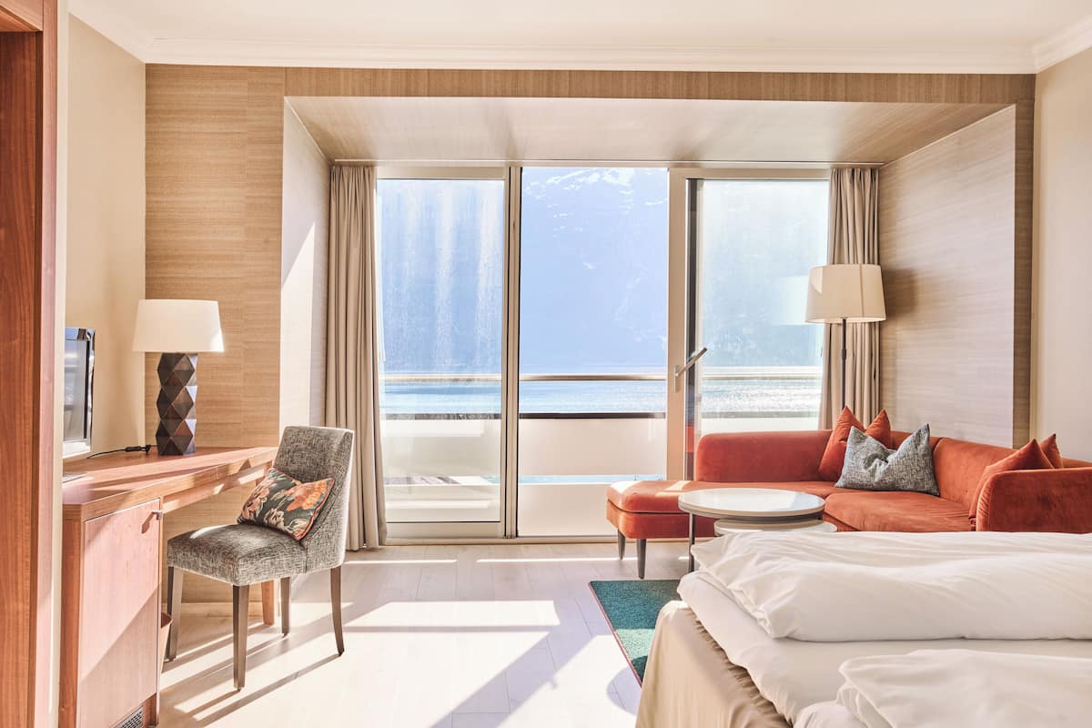 A hotel room with a bed, a desk, a chair, a sofa, and a view of the sea.