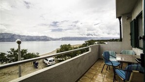 A balcony with a view of a lake and mountains, featuring a table and chairs.