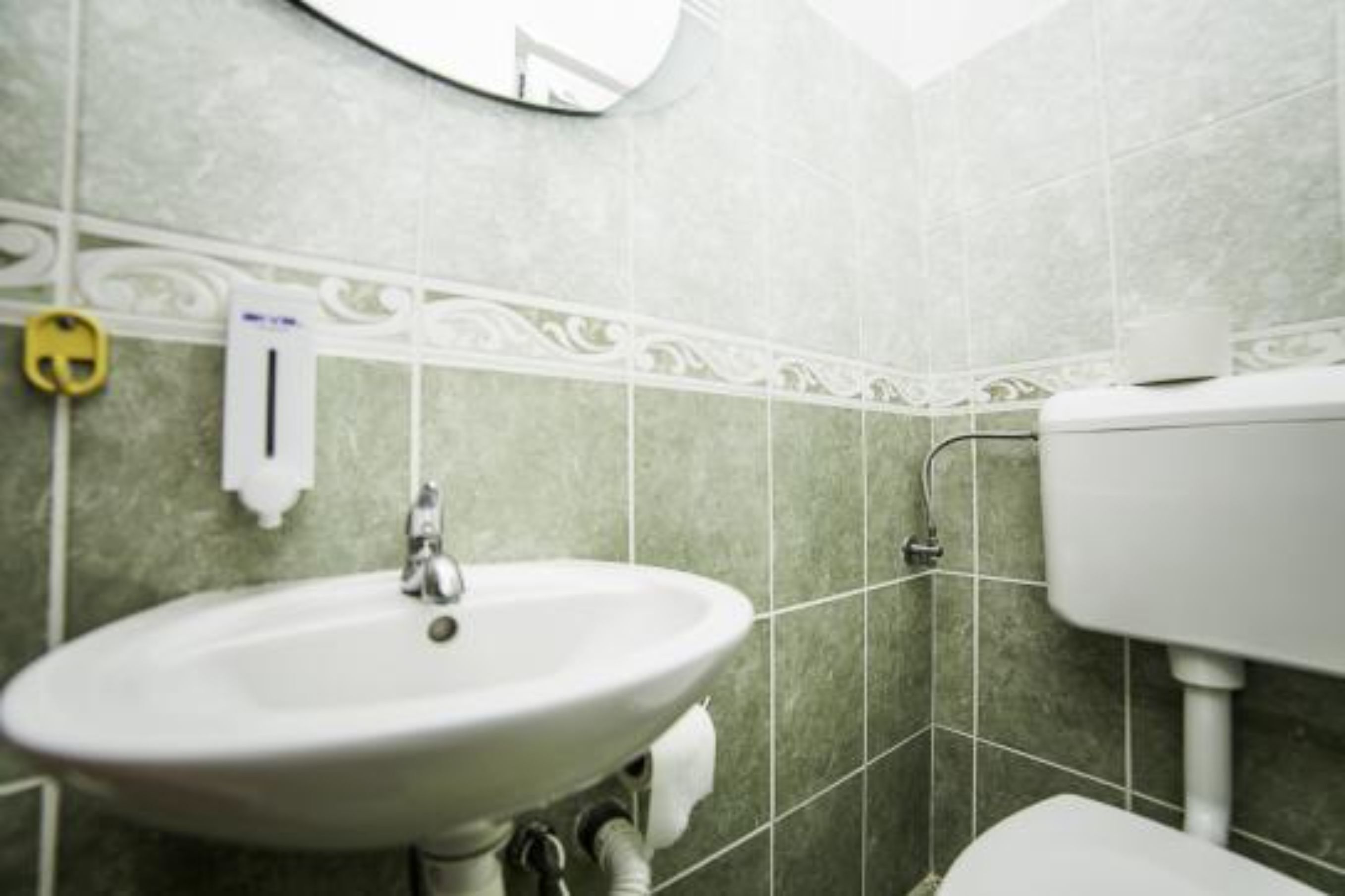 A bathroom with a white sink, a toilet, and green tiles.