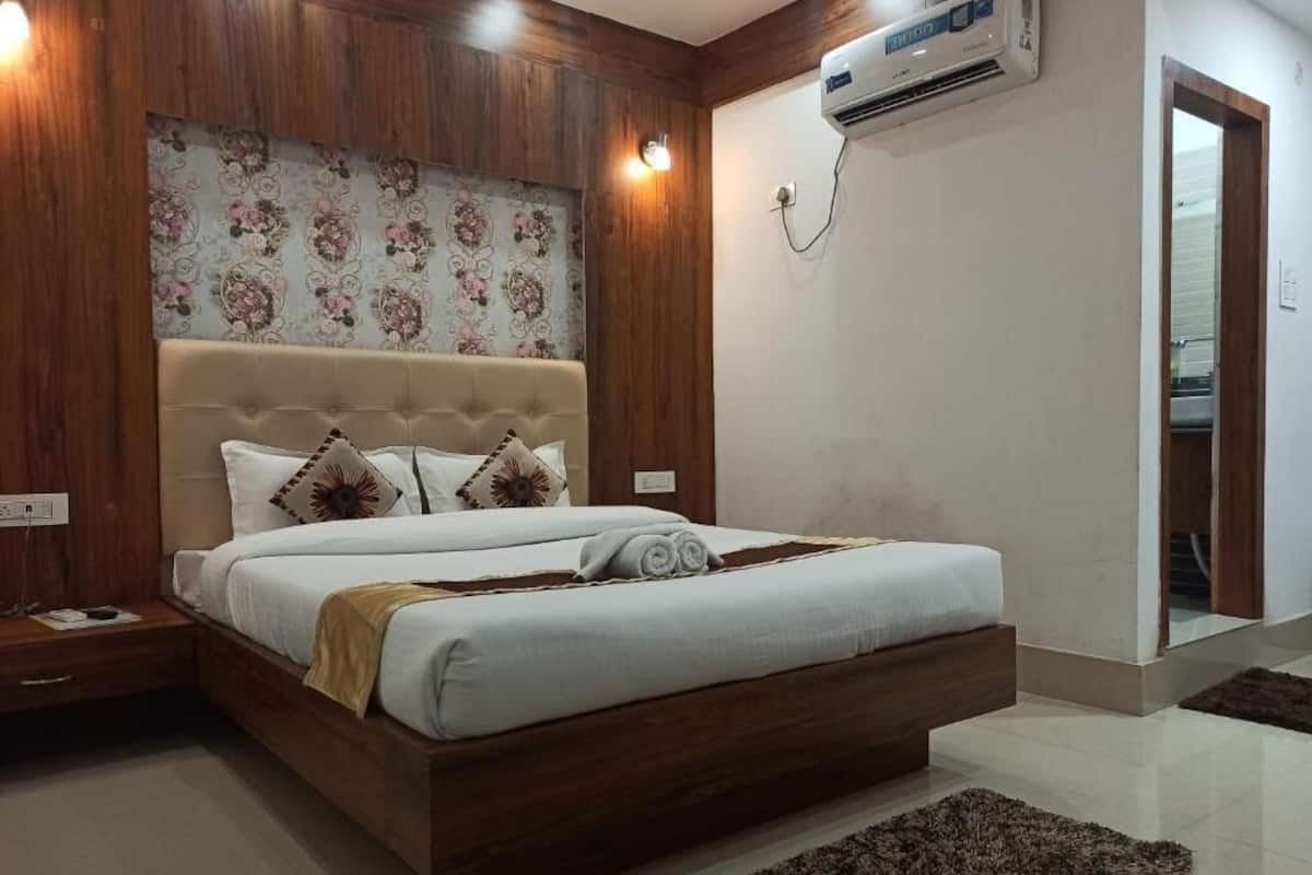 A bedroom with a wooden headboard, a large bed with white bedding, a fluffy rug, and a wall-mounted air conditioner.