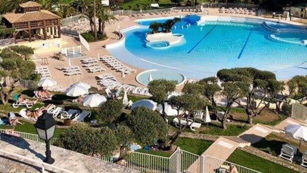 A large swimming pool with a view of the sea, surrounded by lounge chairs and a gazebo.