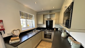 A modern kitchen with stainless steel appliances, a heart-shaped decoration, and a window with a view. - Stunning Coastal Cottage - Sleeping 5 in 2 Bedrooms - Pool and Beach Access Included. (Filey)