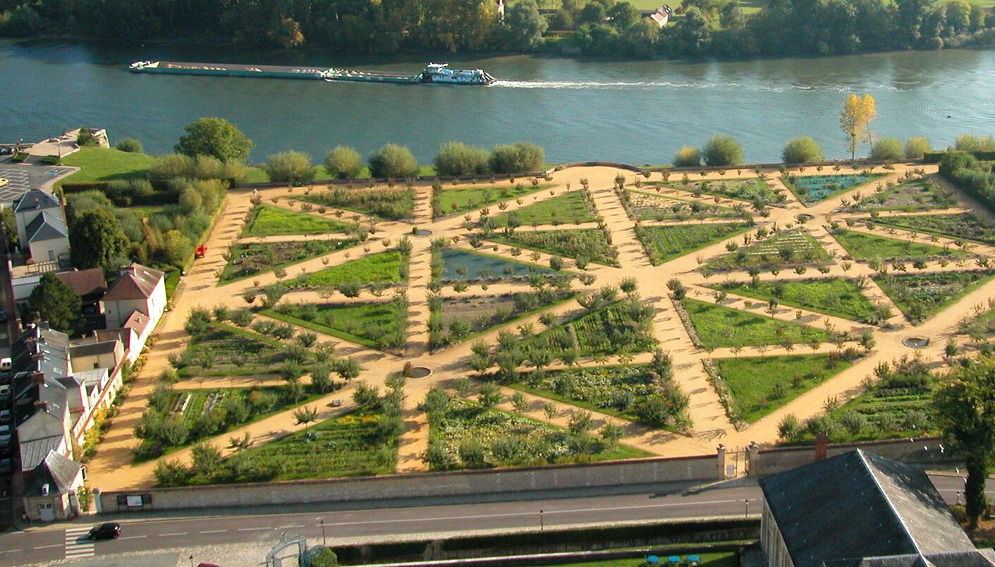 An aerial view of a landscaped garden with geometric patterns, a river in the background, and a bridge.
