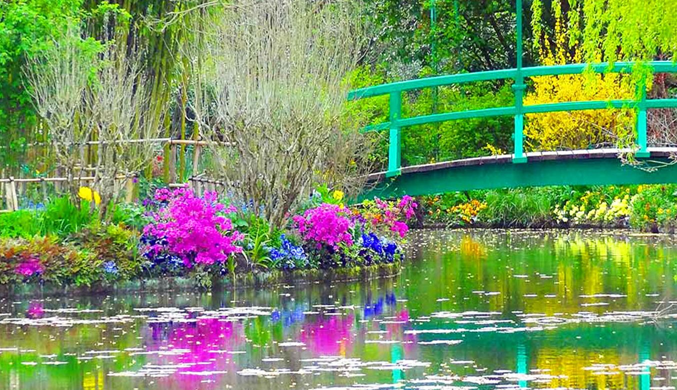 Un ponte verde sopra uno stagno, con fiori colorati e alberi.